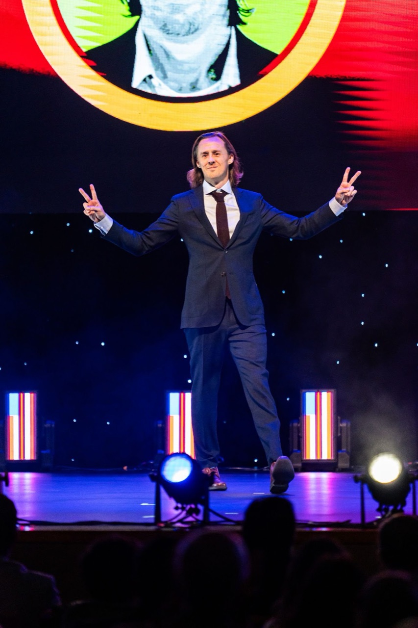 David Wrench on stage at Warrior Rising, flashing peace signs